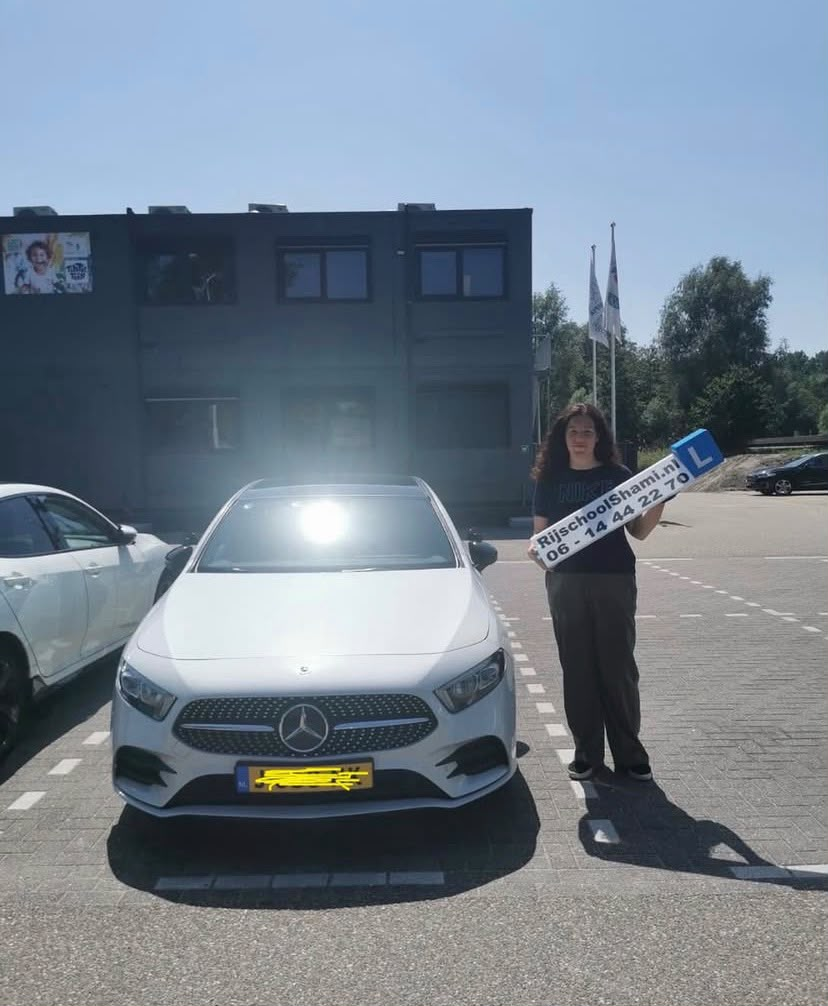 Geslaagde leerling met Rijschool Shami-bord naast de Mercedes A-Klasse lesauto